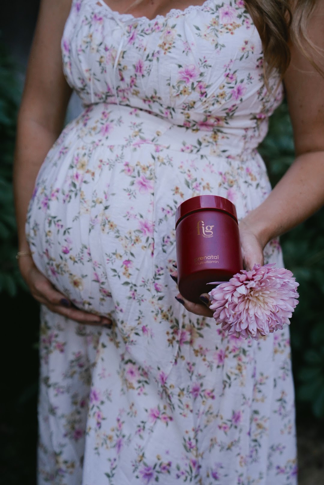 Pregnant woman in a floral dress holding a jar of FIG Prenatal Multi