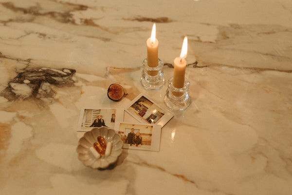 Flat lay of a lit candle, polaroid photos, a fresh fig, and supplement softgels in a small dish on a marble counter